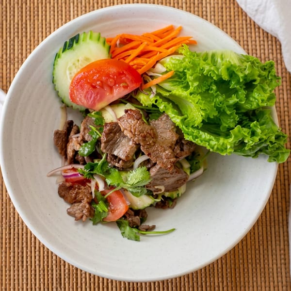 Savory beef salad with fresh greens, cucumber, tomato, and carrots, served with chopsticks.
