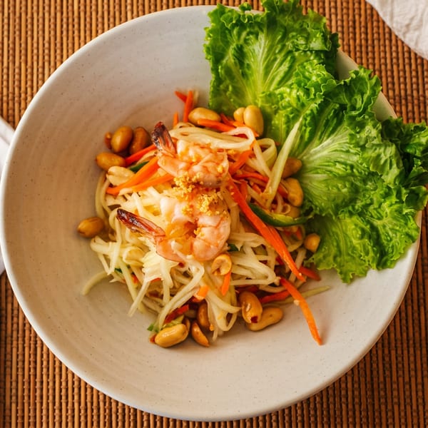 Papaya salad with shrimp, peanuts, carrots, and lettuce, served with chopsticks and spoon.