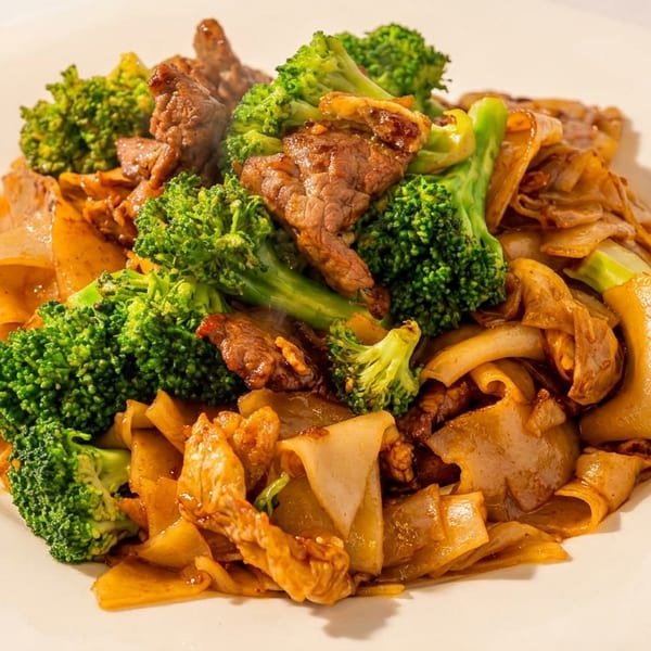 Thai stir-fried wide noodles with beef and fresh broccoli florets on a white plate.