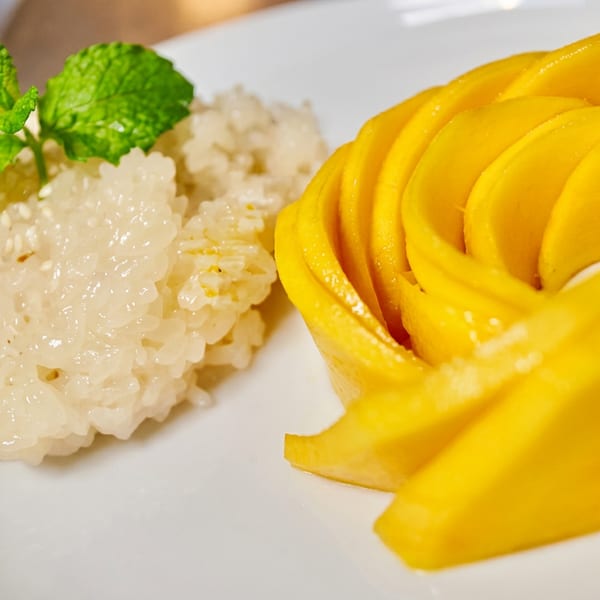 Bright yellow mango slices and sticky rice with mint on a white plate.